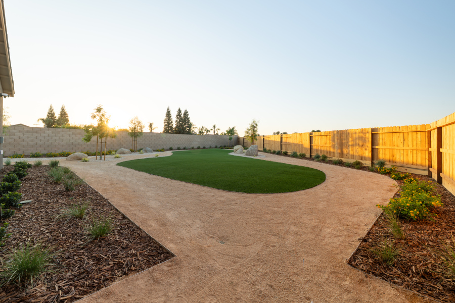 A fenced in yard with a dirt path and grass and trees.