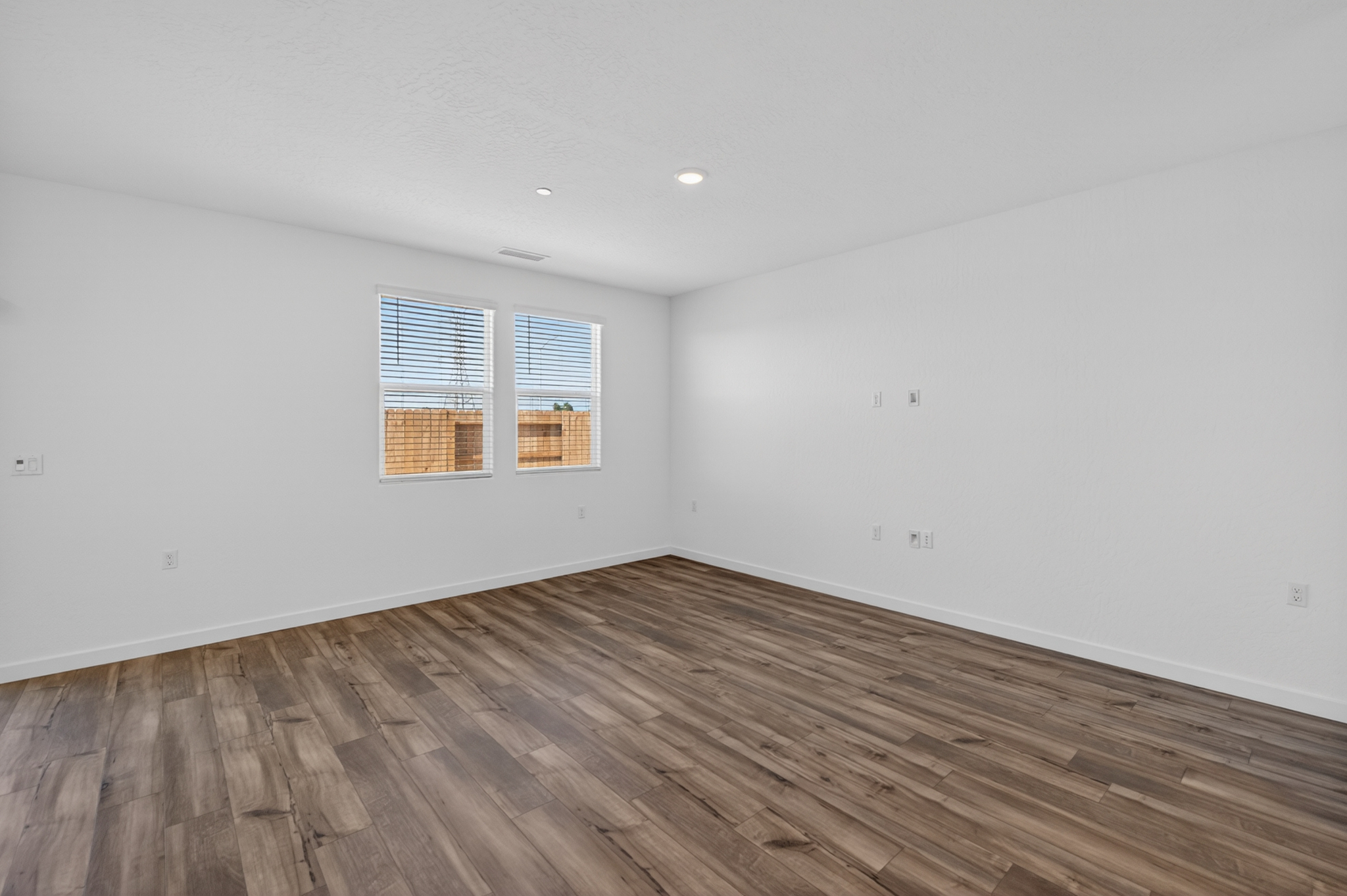 A room with a wood floor and a window with blinds.