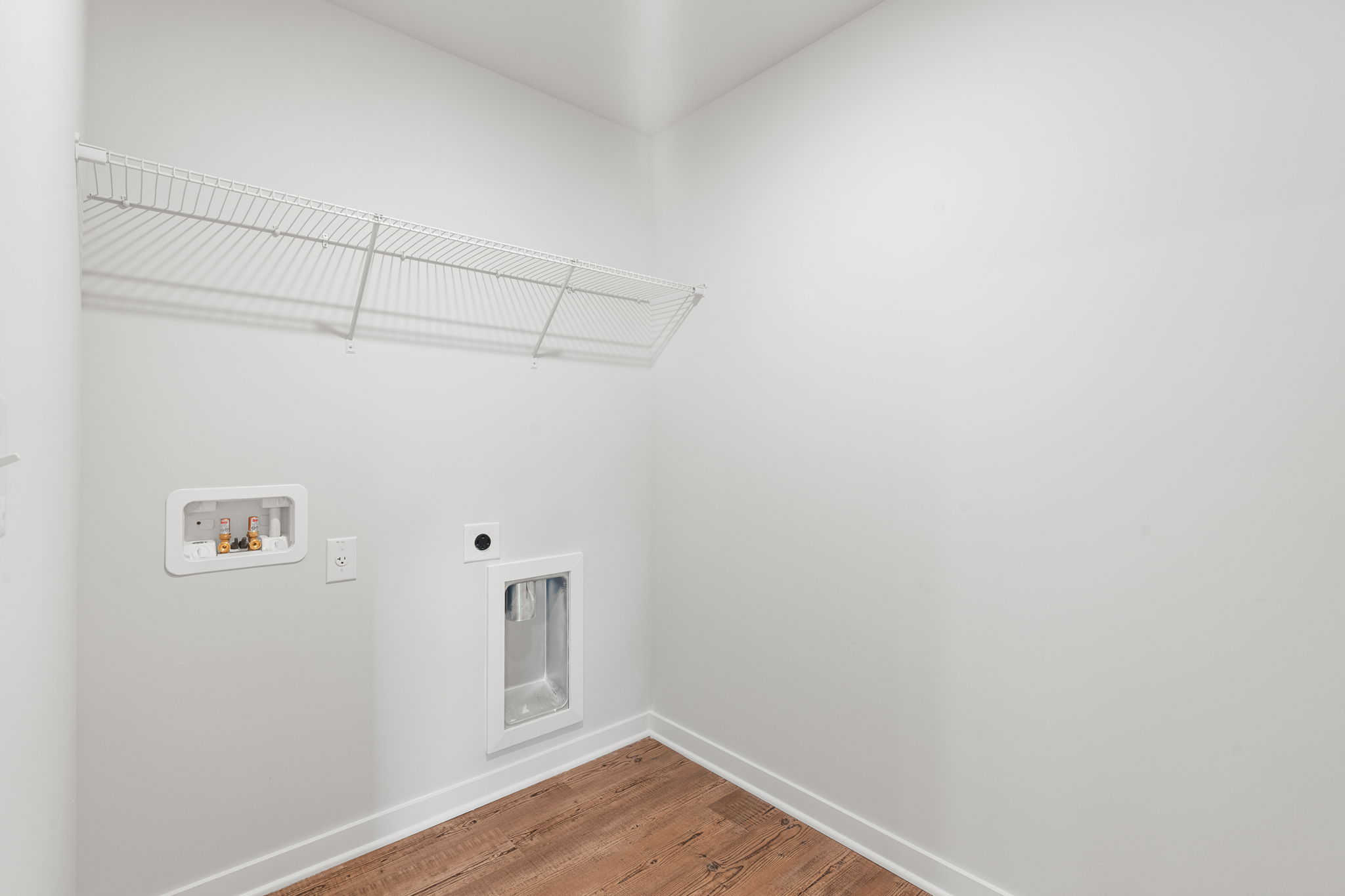 A room with a wood floor and a white wall with a vent.