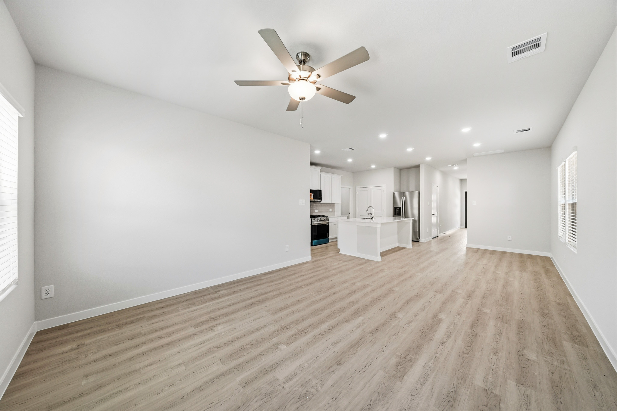 A large empty room with a ceiling fan and a wood floor.