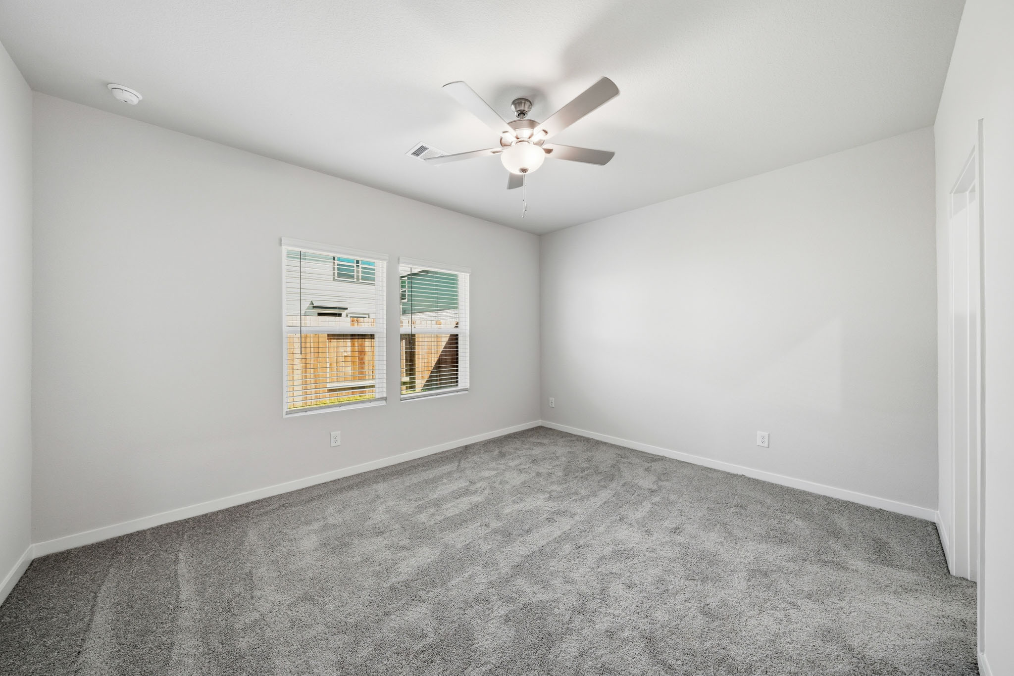 A room with a ceiling fan and a carpet.