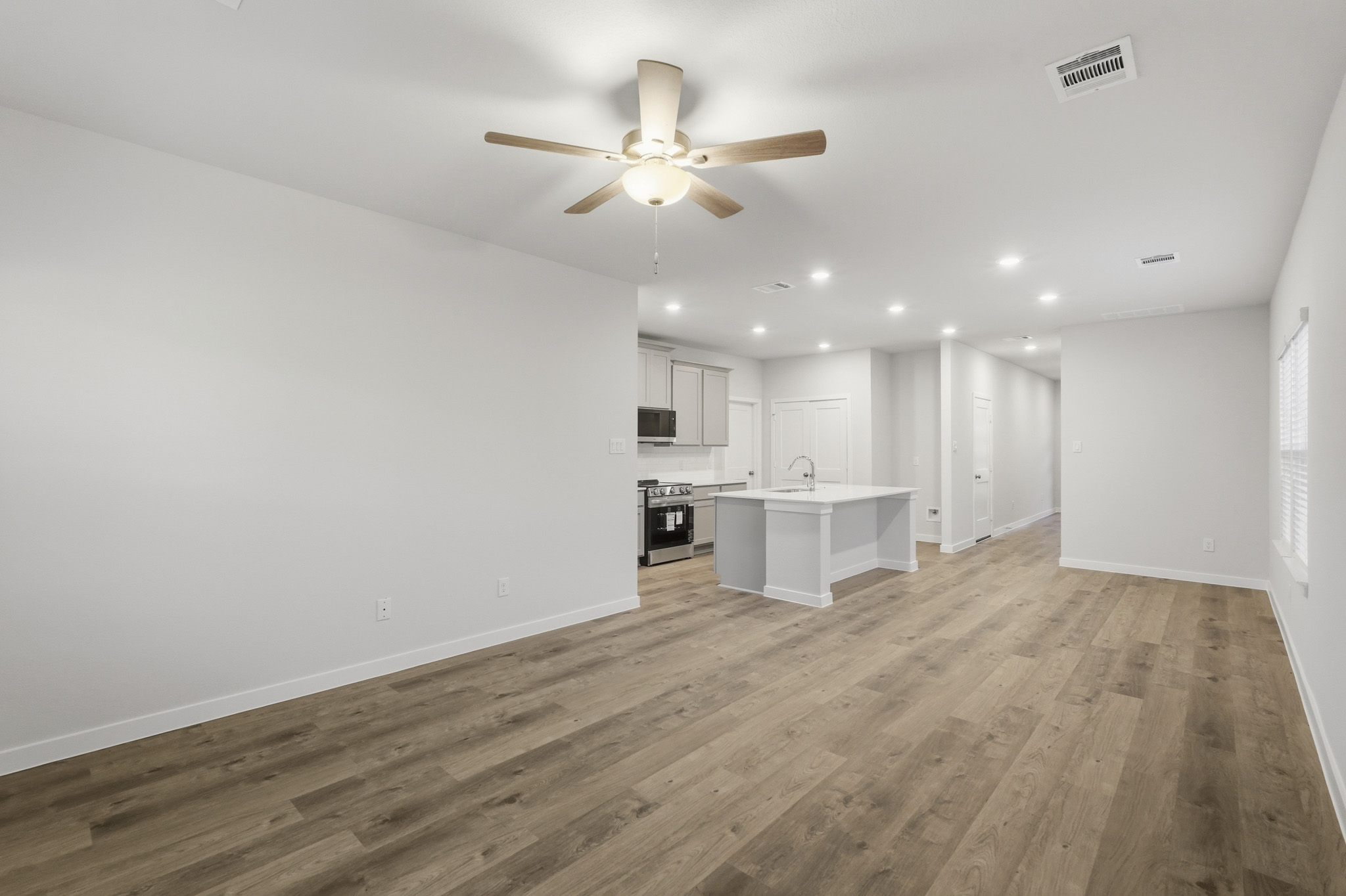 A large empty room with a ceiling fan and a wood floor.