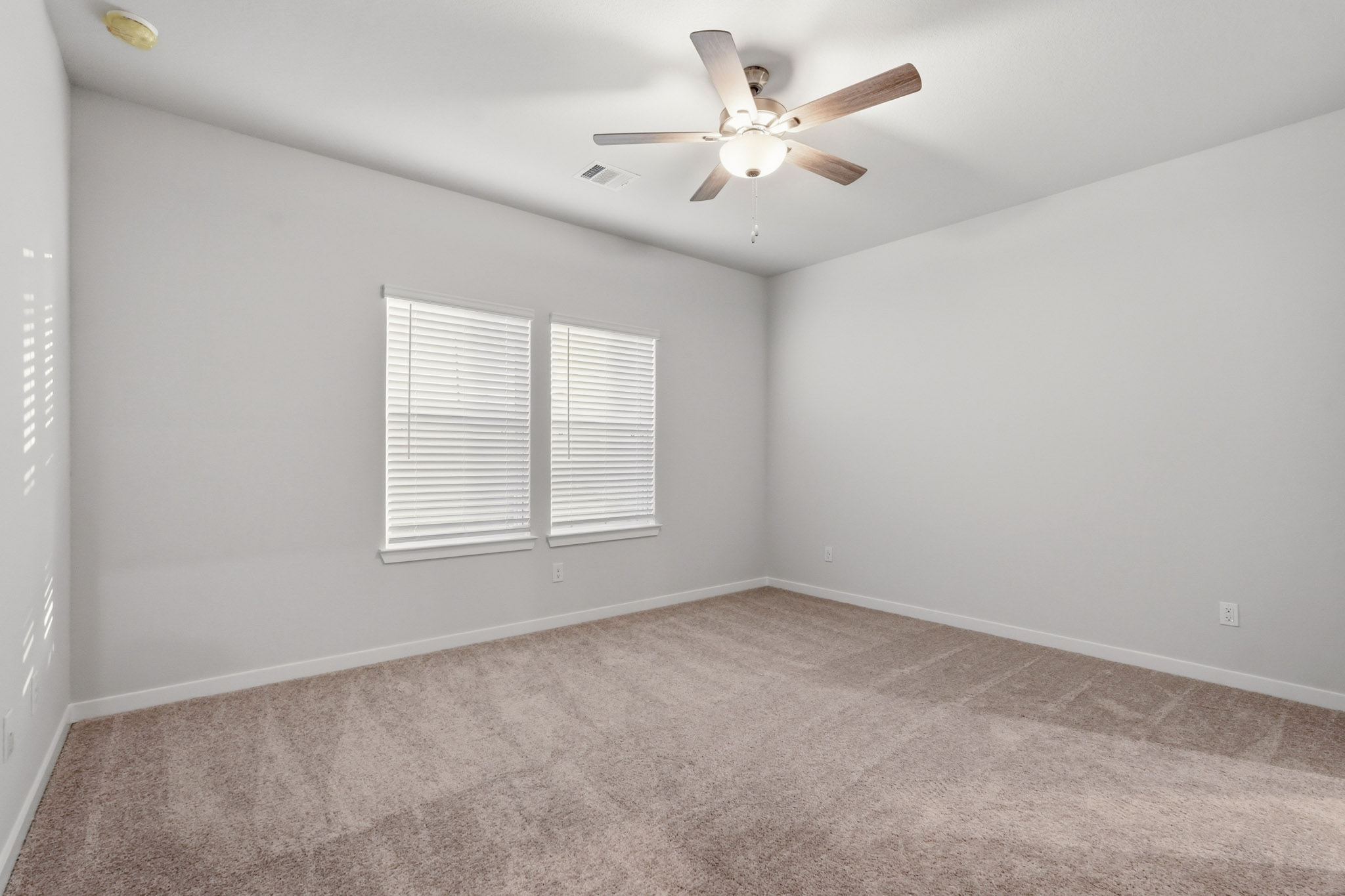 A room with a ceiling fan and a carpet.