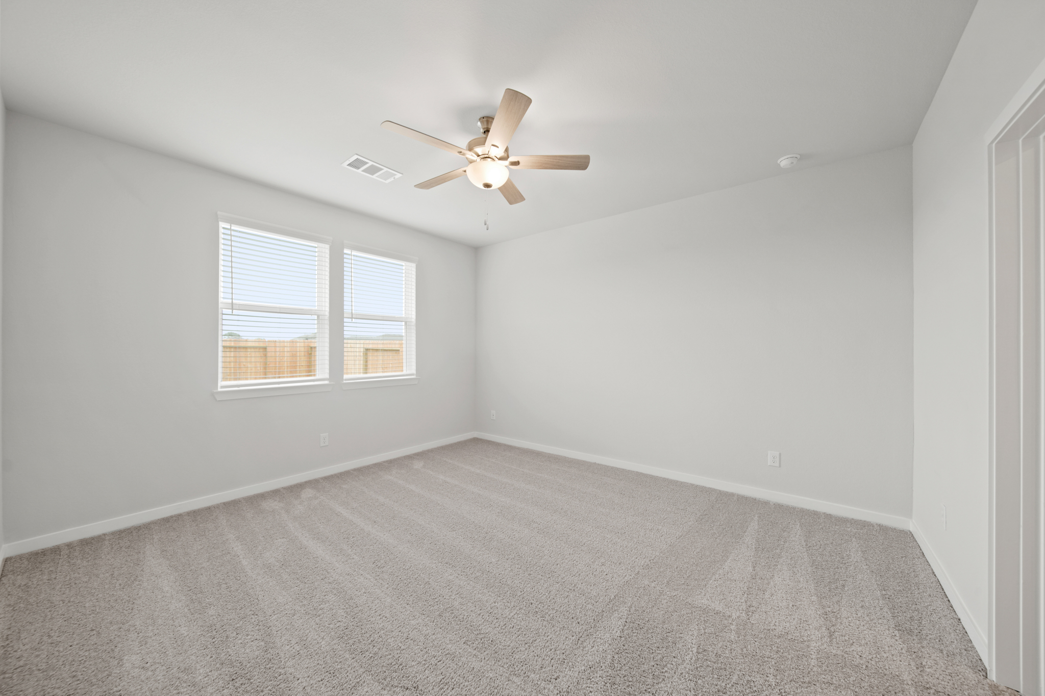 A room with a ceiling fan and a carpet.