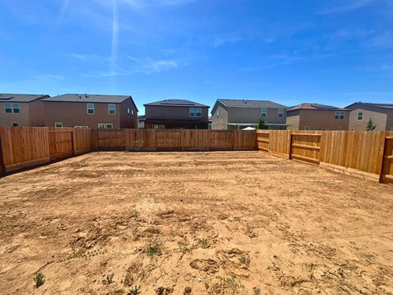 A dirt field with a fence and buildings in the background.
